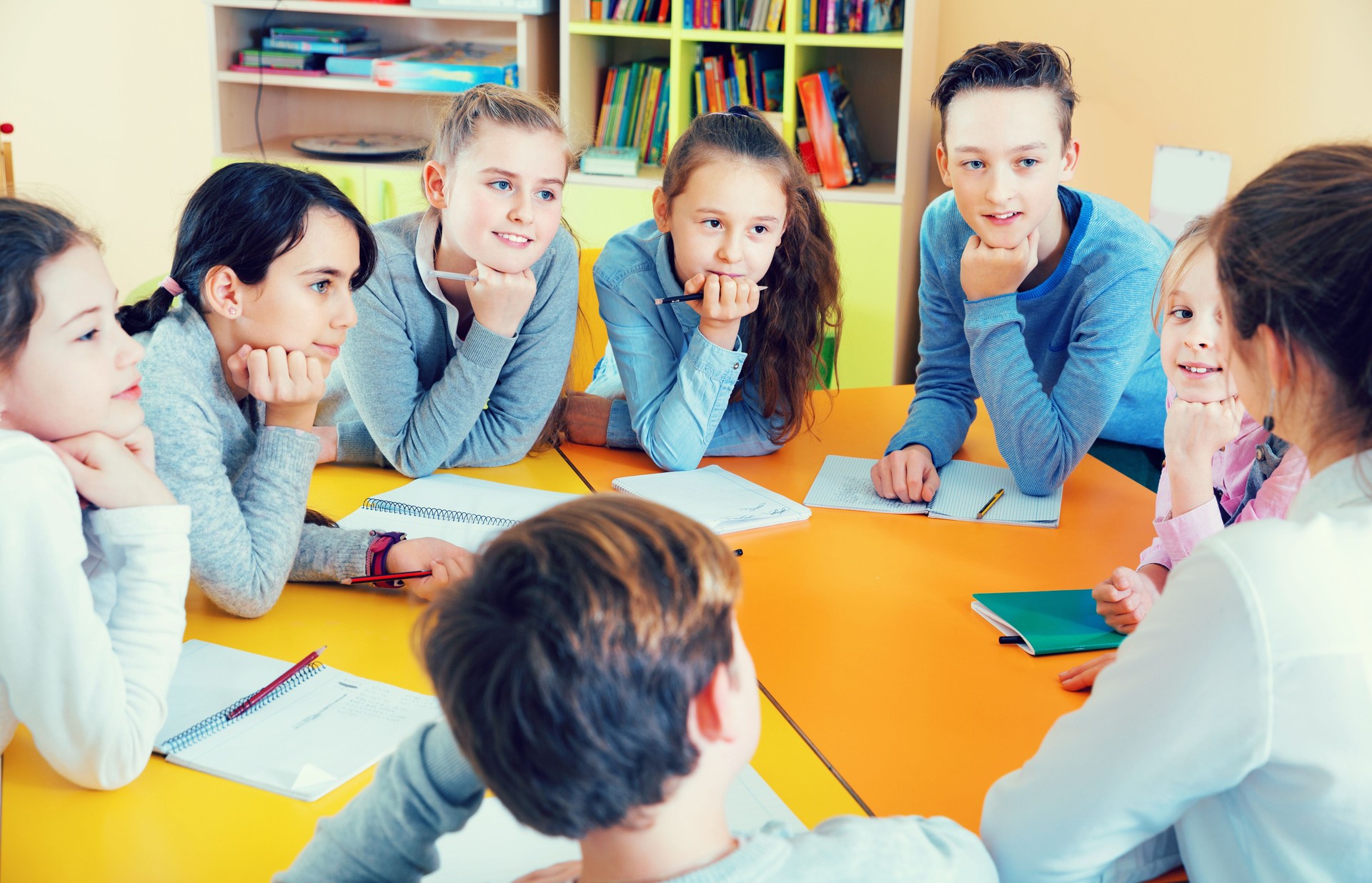Enseignant féminin amical parlant aux enfants, s'asseyant ensemble autour du bureau